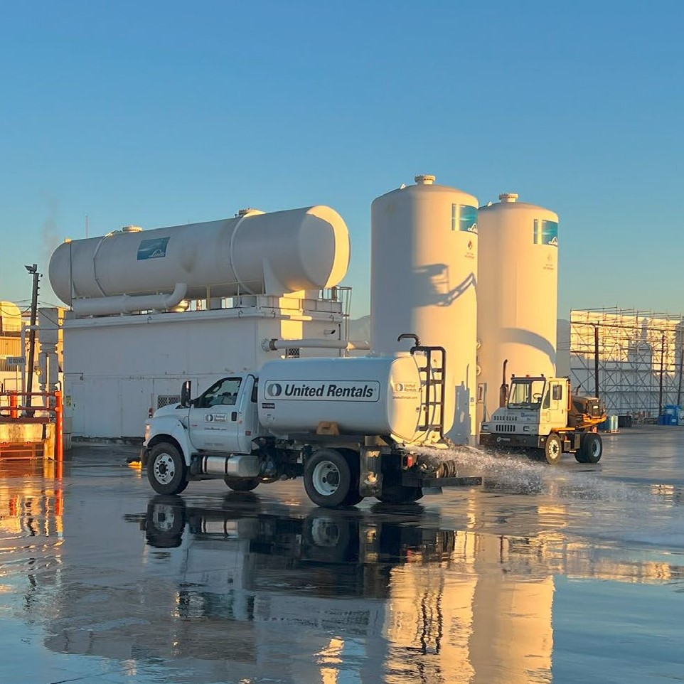 Lead battery recycler with truck spraying water on pavement for a facility washdown to control emissions.