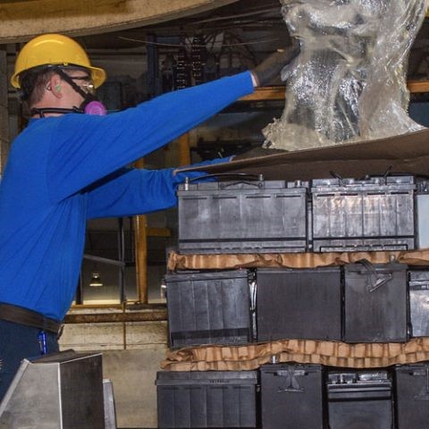 Lead battery recycling employee unwrapping a pallet of spent lead batteries.